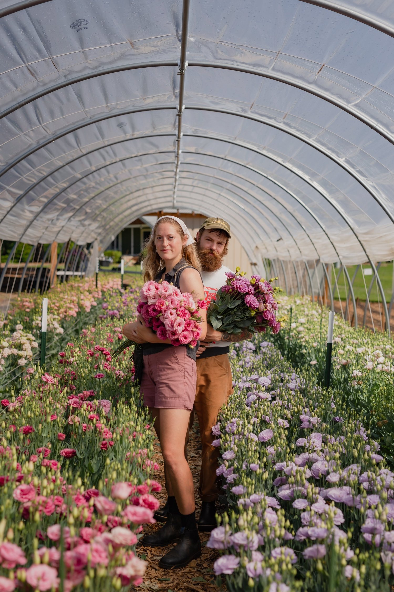 Two guests holding fresh-cut bouquets inside the hoop house